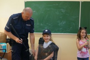 dzieci wspólnie z policjantem przymierzają policyjny sprzęt