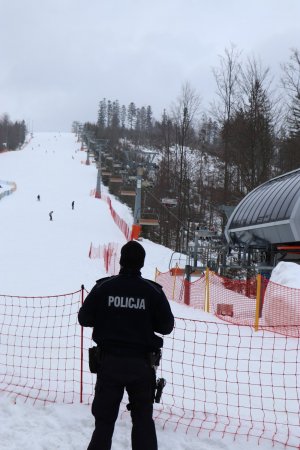 policjant stoi tyłem w tle stok narciarski i wyciąg