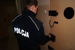policjant zamyka drzwi celi stoi tyłem na plecach widoczny napis policja