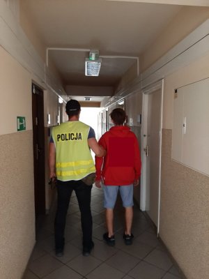 policjant stoi tyłem z zatrzymanym w tle korytarz