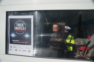 zdjęcie stacji diagnostycznej na wejściu powieszony jest plakat akcji w środku przez szybę widać policjantkę oraz klienta stacji