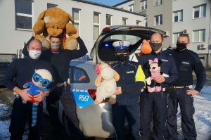 policjanci trzymają zabawki stoją przed radiowozem