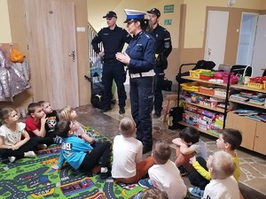 policjantka z dwoma policjantami stoi w sali dzieci siedzą na dywanie