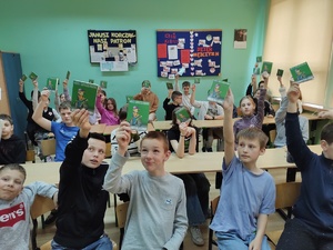 zdjęcie kolorowe uczniowie trzymają w podniesionych do góry rękach książeczki